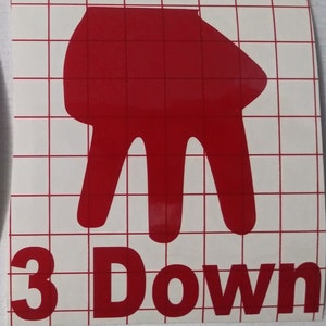 Peut inclure: Un autocollant en vinyle rouge repr&eacute;sentant un geste de la main avec trois doigts pointant vers le bas, au-dessus des mots "3 Down" en rouge. L'autocollant est sur un fond blanc avec un motif quadrill&eacute;.