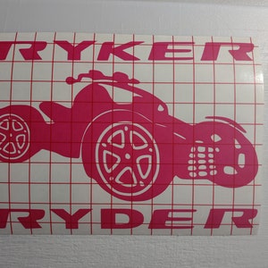 May include: Pink vinyl decal of a three-wheeled car with the word "RYDER" written above and below the car.