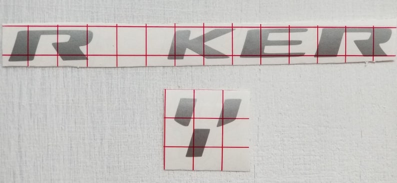 May include: A silver vinyl sticker with the word "RKEIR" in a bold, stylized font. The sticker is on a white background with a grid pattern.