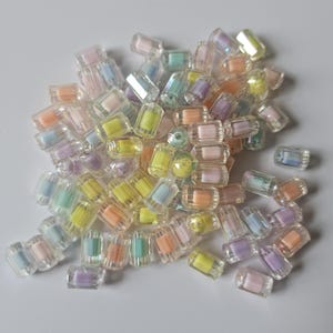May include: A collection of colorful, translucent beads in various pastel shades, including pink, yellow, green, and purple. The beads are rectangular with rounded edges, and some have a slight iridescent sheen. These beads are suitable for jewelry making and crafts.