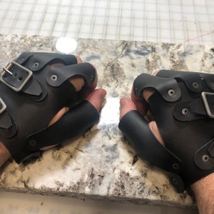 May include: A pair of black leather fingerless gloves with multiple buckles and metal accents.