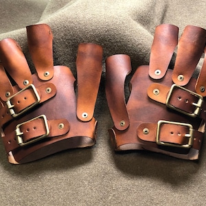 May include: A pair of brown leather fingerless gloves with multiple buckles and brass accents.