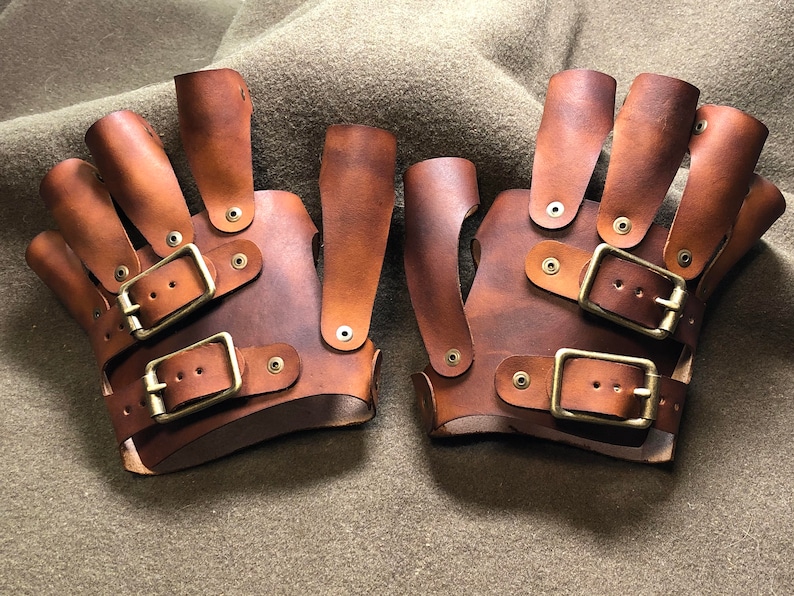 May include: A pair of brown leather fingerless gloves with multiple buckles and brass accents.