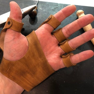 May include: A brown leather fingerless glove with individual finger protection. The glove has a strap that wraps around the wrist.