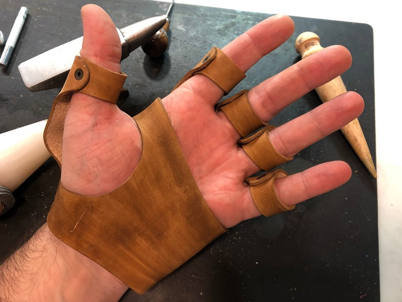May include: A brown leather fingerless glove with individual finger protection. The glove has a strap that wraps around the wrist.