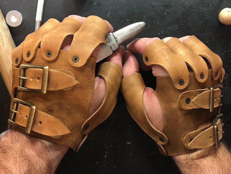 May include: A pair of brown leather fingerless gloves with buckles and rivets. The gloves are worn on a person's hands.