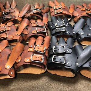 May include: A group of leather fingerless gloves with buckles. Some are brown and some are black.