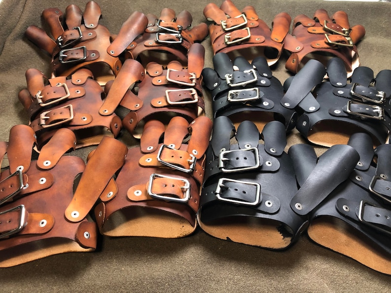 May include: A group of leather fingerless gloves with buckles. Some are brown and some are black.