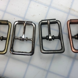 May include: Four metal belt buckles in different finishes: brass, silver, gunmetal, and copper.