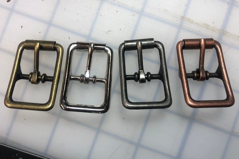 May include: Four metal belt buckles in different finishes: brass, silver, gunmetal, and copper.