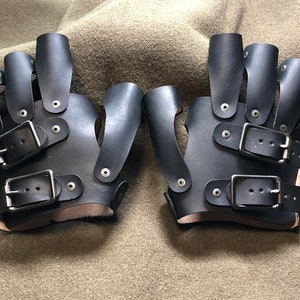 May include: A pair of black leather fingerless gloves with multiple buckles and straps. The gloves have a unique design with finger holes and a wrist strap.