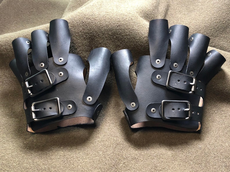 May include: A pair of black leather fingerless gloves with multiple buckles and straps. The gloves have a unique design with finger holes and a wrist strap.