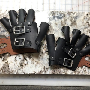 May include: Two pairs of black leather fingerless gloves with multiple buckles and straps. The gloves have a brown leather wrist strap.