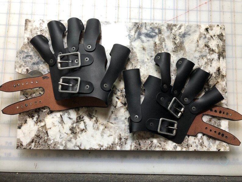 May include: Two pairs of black leather fingerless gloves with multiple buckles and straps. The gloves have a brown leather wrist strap.