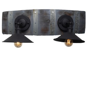 Puede incluir: Una lámpara de pared de madera rústica con dos apliques de metal negro. La lámpara está hecha de madera reciclada y tiene un acabado desgastado. Cada aplique tiene una pantalla de metal negro y una bombilla de vidrio transparente.