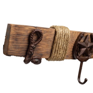 Pu&ograve; includere: Un gancio da parete in legno rustico con un dettaglio in corda e tre ganci in metallo. I ganci sono a forma di ferro di cavallo, stella e corda attorcigliata.