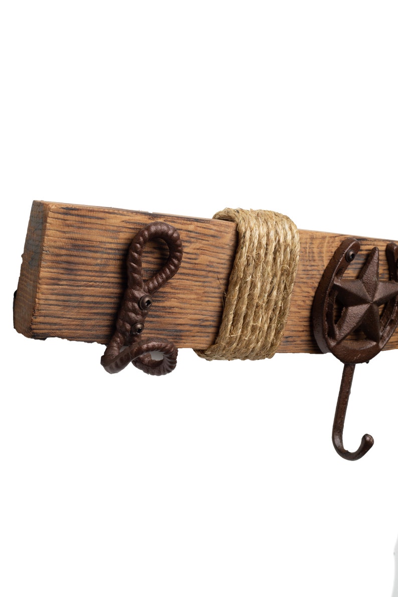 Pu&ograve; includere: Un gancio da parete in legno rustico con un dettaglio in corda e tre ganci in metallo. I ganci sono a forma di ferro di cavallo, stella e corda attorcigliata.