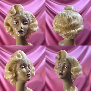 May include: A blonde wig with a vintage style, featuring large, curled waves and a bouffant. The wig is styled on a mannequin head, with the back of the wig visible in the image.