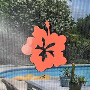Könnte beinhalten: Ein leuchtend orangefarbener Hibiskus-Blumen-Ausschnitt an einer Fliegengittertür. Die Blume ist scharf, während der Hintergrund unscharf ist und einen Swimmingpool, Gartenmöbel und grüne Bäume zeigt.