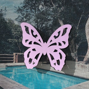May include: A light purple butterfly cutout with intricate details. The butterfly is against a background of a screen door with a swimming pool visible in the background.