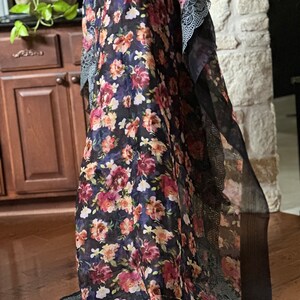 May include: A black sheer scarf with a floral print and lace trim. The scarf has a dark background with pink, red, and yellow flowers.