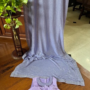 Pode incluir: Uma blusa sem mangas de cor lil&aacute;s claro com uma gola branca e um tecido de lantejoulas no fundo.