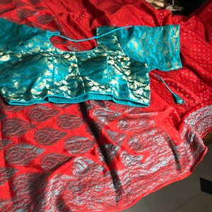 May include: A red and silver patterned saree with a turquoise and gold embroidered blouse. The saree has a decorative border.
