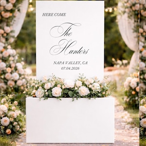 May include: Two wedding signs, one white and one black, with floral arrangements. The white sign reads "Here Come The Hunters" with the date and location. The black sign says "Welcome to the Wedding of Olivia and Daniel" with the wedding date.