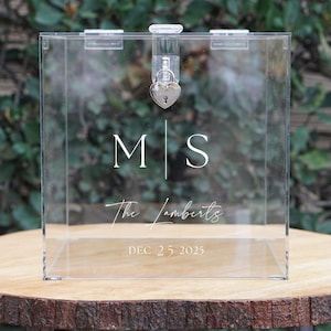May include: Clear acrylic box with a heart-shaped lock and keyhole. The box has the initials "M|S" and the text "The Lamberts" and "DEC 25 2025" printed on it.