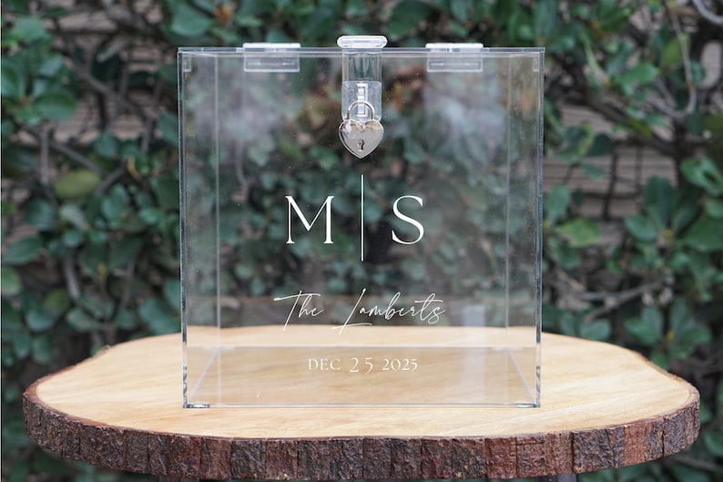 May include: Clear acrylic box with a heart-shaped lock and keyhole. The box has the initials "M|S" and the text "The Lamberts" and "DEC 25 2025" printed on it.
