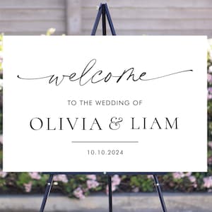 May include: White wedding welcome sign with black calligraphy text that reads "welcome to the wedding of Olivia & Liam 10.10.2024".