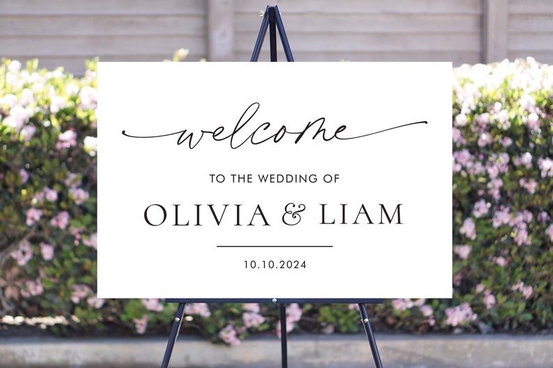 May include: White wedding welcome sign with black calligraphy text that reads "welcome to the wedding of Olivia & Liam 10.10.2024".
