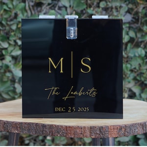 May include: Black acrylic box with a gold inscription. The inscription reads "M|S The Lamberts DEC 25, 2025".