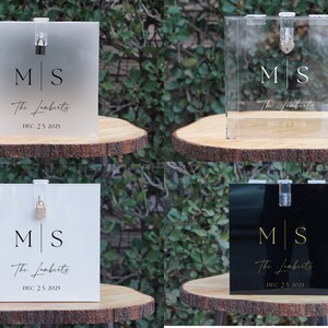 May include: Four acrylic wedding card boxes with different finishes. The boxes are clear, frosted, white, and black. Each box has a lock and key, and is decorated with the initials "M|S" and the text "The Lomberts" and "DEC 25 2025".