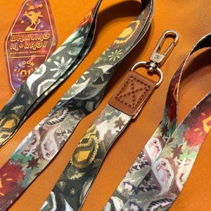 Puede incluir: Primer plano de varios cordones estampados y un llavero. Los cordones presentan un diseño floral y geométrico repetido en tonos verdes, marrones y rojos. El llavero tiene el texto "Whirling in Rags" y un número de habitación.