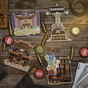 May include: An assortment of embroidered patches featuring building designs and the text "The Ultra Luxe", "Lucky 38", "Gomorrah", and "The Tops". Also shown are bottle caps, bullets, playing cards, and a Sunset Sarsaparilla sign.