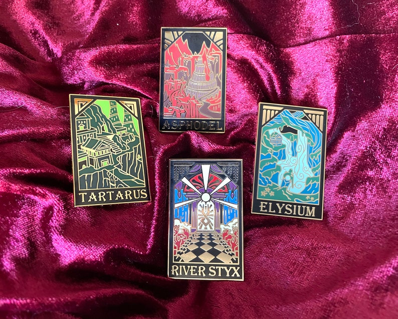May include: Four rectangular enamel pins with gold borders. Each pin features a different illustrated scene with text: "TARTARUS", "ASPHODEL", "ELYSIUM", and "RIVER STYX". The pins are set against a deep red velvet background.