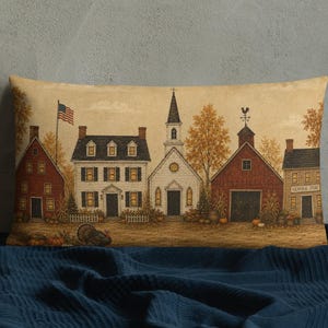 May include: A rectangular throw pillow featuring a printed illustration of a small town scene during autumn. The design includes a white church, red barns, and houses with an American flag, surrounded by orange trees and pumpkins on a tan background.