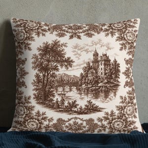 May include: A square throw pillow featuring a brown and white toile de jouy pattern. The central illustration depicts a landscape with a castle, a bridge, and figures near water, framed by a decorative floral border on a cream-colored background.