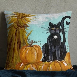 Peut inclure: Coussin carré décoratif avec un chat noir assis sur des citrouilles oranges. Le motif peint comprend un fond bleu clair, une botte de foin et un thème automnal. Article décoratif.