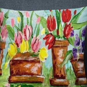 May include: A colorful pillow featuring a painting of tulips in terracotta pots. The tulips are pink, red, yellow, and orange. The background is a light blue.