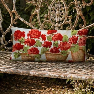 May include: A rectangular throw pillow featuring a vibrant print of red geranium flowers in terracotta pots. The pillow is positioned on a weathered, ornate white metal garden bench with intricate scrollwork and a distressed finish.