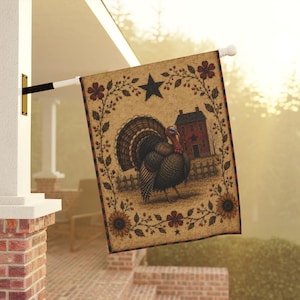 May include: A rectangular garden flag featuring a central illustration of a turkey standing in front of a red house and a wooden fence. The design is framed by a border of brown vines, red flowers, and sunflowers, with a black star at the top center.