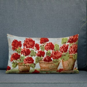 May include: A rectangular throw pillow with a vintage-style illustration of three potted red geraniums. The flowers are painted in a watercolor style with green leaves and brown pots.