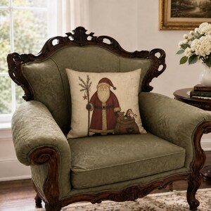 May include: A square throw pillow featuring a printed illustration of Santa Claus wearing a red coat and hat, holding a staff with a star, and carrying a sack filled with toys, set against a light beige background with a textured appearance.