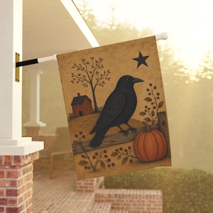 May include: A rectangular garden flag featuring a black crow perched on a wooden fence. The scene includes a small red house, a bare tree, a pumpkin, and a black star against a tan background with berry sprigs. The flag hangs from a white pole.