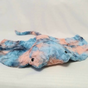 May include: A plush toy shaped like a blue and pink stingray. The toy has a marbled pattern and black eyes.