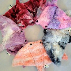 May include: A collection of plush stingray toys in various colors, including red, pink, purple, and gray. Each toy has button eyes and a tag. The toys are arranged in a circular pattern.