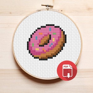 May include: A pink and brown pixelated donut with colorful sprinkles. The donut is in a white embroidery hoop.