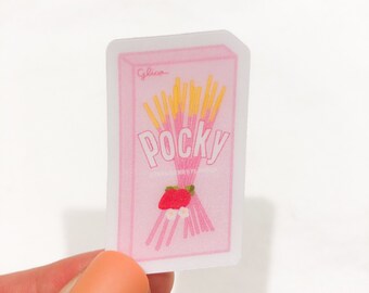 Puede incluir: Una pegatina rosa que representa una caja de Pocky de fresa. El diseño incluye la palabra "Pocky", una ilustración de fresa y la marca "Glico". La pegatina se sostiene sobre un fondo blanco.
